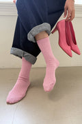 Person wearing pink socks and holding pink high heels on a neutral background