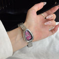 Hand wearing a silver watch with a purple face on a white background