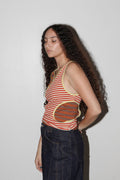 Woman wearing a red and white striped tank top with a graphic design, standing against a plain background.