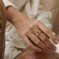 A brass ring with gold tones, featuring a series of unakite stones in various shapes including circle and square, set within metallic frames.