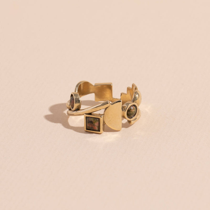 A brass ring with gold tones, featuring a series of unakite stones in various shapes including circle and square, set within metallic frames.