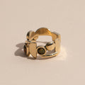 A brass ring with gold tones, featuring a series of unakite stones in various shapes including circle and square, set within metallic frames.