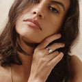 Woman wearing brass ring with gold tones, featuring a series of unakite stones in various shapes including circle and square, set within metallic frames.