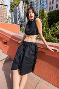 Woman in a black outfit standing on a rooftop with cityscape and plants in the background