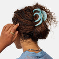 Person with braided hair using a turquoise hair clip on a white background