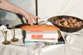 Person cutting bread on a book with a bowl of potatoes nearby