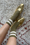 Gold flats and green socks with white stripes on a textured surface