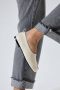 White flat shoe worn with gray jeans on a light gray background