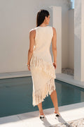 Woman in a beige fringe dress standing by a pool with a modern architectural background