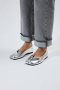 Silver metallic shoes worn with rolled-up gray jeans on a white background.