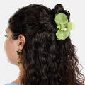 Woman with wavy hair wearing a green flower hair accessory on a white background