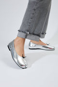 Silver metallic shoes worn with gray jeans on a neutral background