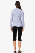 A woman viewed from the back wearing a light blue textured long-sleeve blouse and black cropped pants against a plain white studio background.