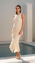 Woman wearing a white fringe dress standing in a minimalist outdoor setting.