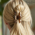 Close-up of a person with blonde hair tied back using a decorative hair clip, with 'French Amie' branding.
