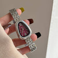 Silver watch with a pink face held by a hand against a neutral background