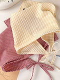 Two gingham-patterned bonnets, one yellow and one red, on a white surface.