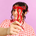 Person wearing a red bow-shaped hair clip against a pink background