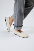 White flat shoes worn with gray jeans on a light gray background
