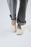 Person wearing white shoes and gray jeans on a light gray background