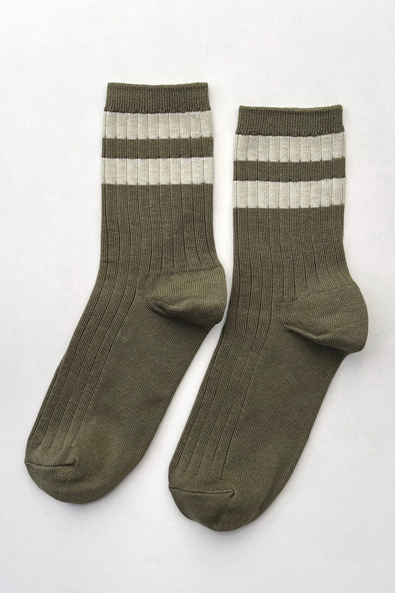 A pair of ribbed crew socks in olive green with two horizontal cream stripes near the cuff, displayed on a light gray background.