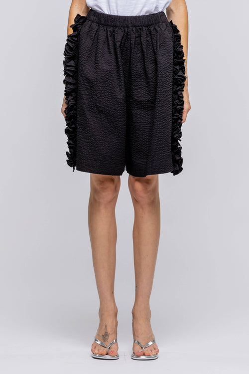 Person wearing black ruffled shorts on a white background