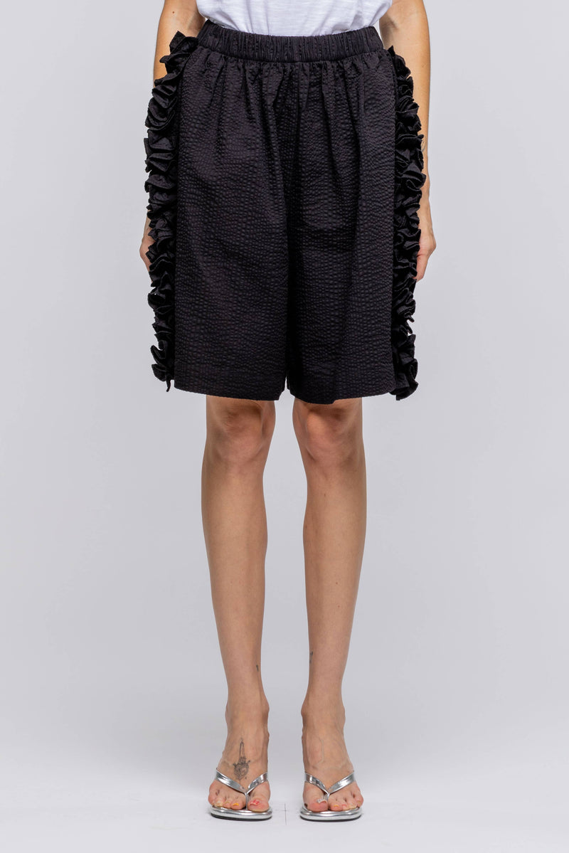 Person wearing black ruffled shorts on a white background
