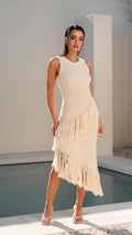 Woman wearing a beige fringe dress standing by a poolside.