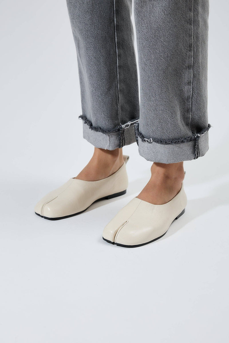 White tabi shoes worn with rolled-up gray jeans on a white background