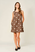 Woman wearing a brown dress with white polka dots on a plain background