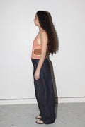 Woman wearing a striped tank top and dark pants against a white wall.