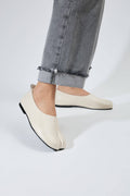 White loafers worn with rolled-up jeans on a light gray background