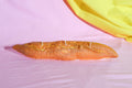 Long, thin, orange-colored object on a pink surface with a yellow fabric in the corner.