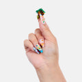 Hand with colorful nail art holding a small figurine against a white background