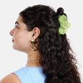 Woman with long dark hair styled in a ponytail with a green flower, wearing gold earrings and a blue top.