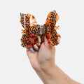 Hand holding a large, decorative hair bow with leopard print and colorful accents on a white background