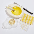 White ceramic bowl with yellow interior, black chopsticks with white patterns, glass container, and floral-patterned paper on a light gray background.
