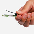 A close-up of a hand holding a small black hair clip with a clear, transparent lower section showing green circuitry inside, set against a plain white background.