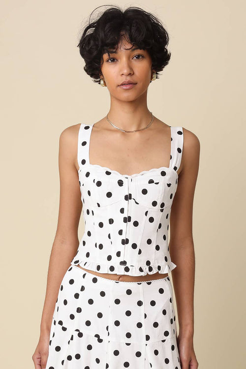 Woman wearing a white sleeveless top with black polka dots against a beige background