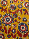 A close-up of a mustard yellow fabric featuring a hand-block printed floral pattern in red, navy blue, and cream.