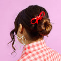 Person with a red hair bow in their hair against a pink background