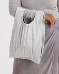 Person holding a pleated gray bag against a light background