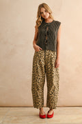 Woman wearing a sleeveless knitted top and leopard print pants against a beige background