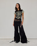 A model stands in a studio wearing a black short-sleeve crop top with a cream floral and star pattern, paired with black wide-leg pants featuring ruching and a belt.