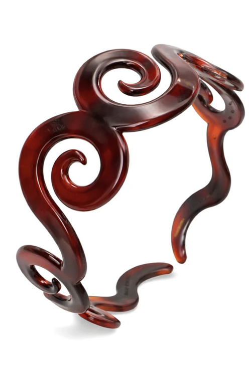 A sculptural open cuff bracelet made of glossy, dark reddish-brown tortoiseshell resin, featuring organic swirls and wavy lines, shown on a plain white background.