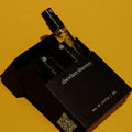 A 2ml sample vial of 'elsewhere discovery' eau de parfum with a black spray nozzle, presented inside its black cardboard packaging box on a solid yellow background.