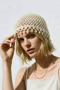 Woman wearing a beige crochet hat with pearl embellishments against a light background