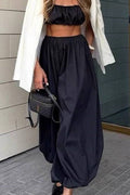 Person wearing a black strapless top and wide-leg pants with a white blazer, standing against a tiled wall.
