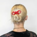 Person with blonde hair tied in a bun with a red hair clip on a white background