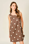Woman wearing a brown dress with white polka dots on a plain background